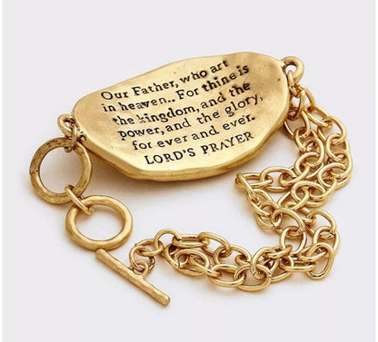 Gold tone toggle bracelet stamped with "Lord’s Prayer " on a silver tone cross on the front, and the Lord’s prayer stamped on the back